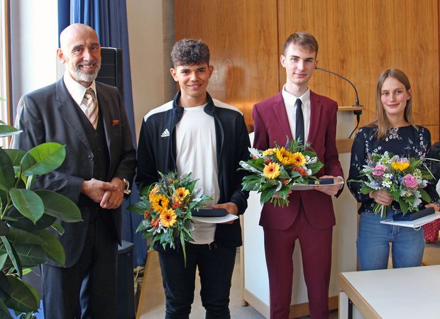 Oberbürgermeister Alexander Ahrens steht neben zwei jungen Männern und einer jungen Frau, die Blumensträuße in der Hand halten