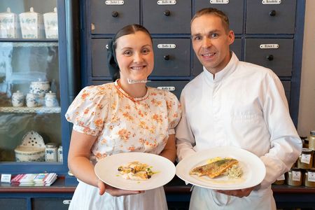 Wjelbik Familie Lukasch Frau in sorbischer Tracht und Mann in weißer Kochkleidung halten Teller mit Essen in der Hand
