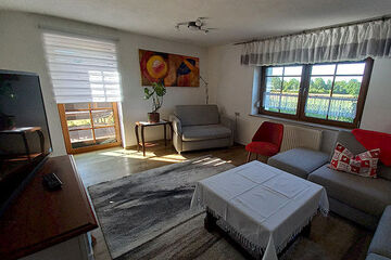 Pension Jokusch Wohnzimmer: TV und braunes Sideboard, gerade zu in der Ecke grauer Sessel und rechts graue Eckcouch davon Couchtisch