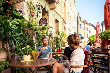 An verschiedenen Tischen sitzen Leute und reden, an der Wand hängen viele Pflanzen