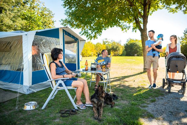 Stausee Campingplatz Junge Familie mit Kinderwagen läuft an Personen mit Hund vorbei welche vor dem Pavillion sitzen