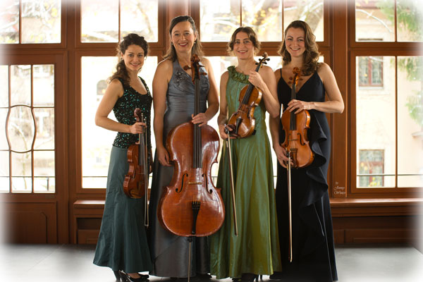 Lunus-Quartett die vier Musikerinnen stehen vor einer großen Fensterfront, sie tragen festliche Kleider, in der Hand halten sie ihre Streichinstrumente